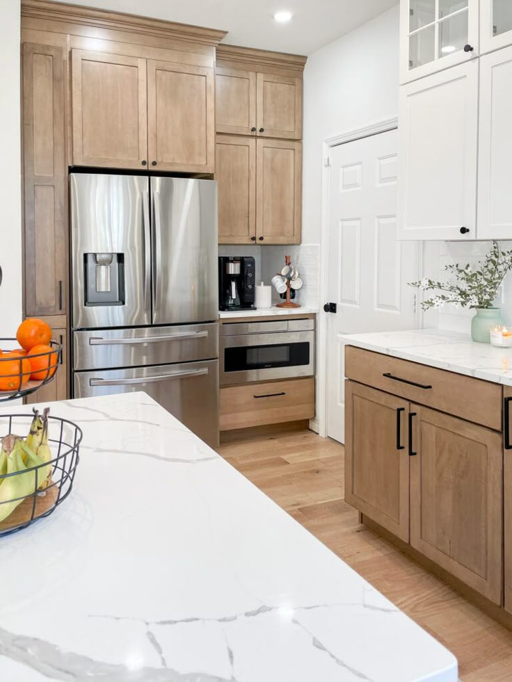 a large kitchen with stainless steel appliances and wooden cabinets, along with white marble countertops