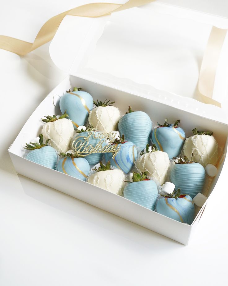 blue and white chocolate covered strawberries in a box with gold ribbon on the side