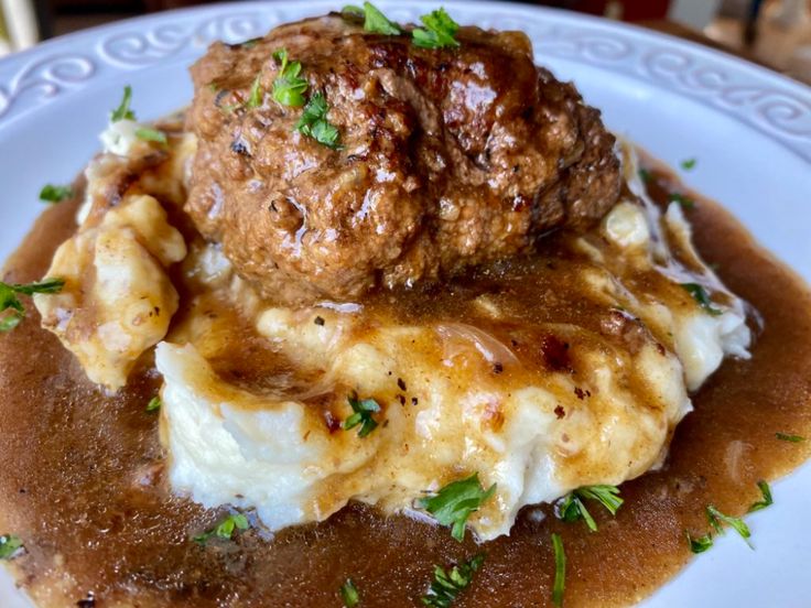 meatballs and mashed potatoes on a white plate with gravy, garnished with parsley