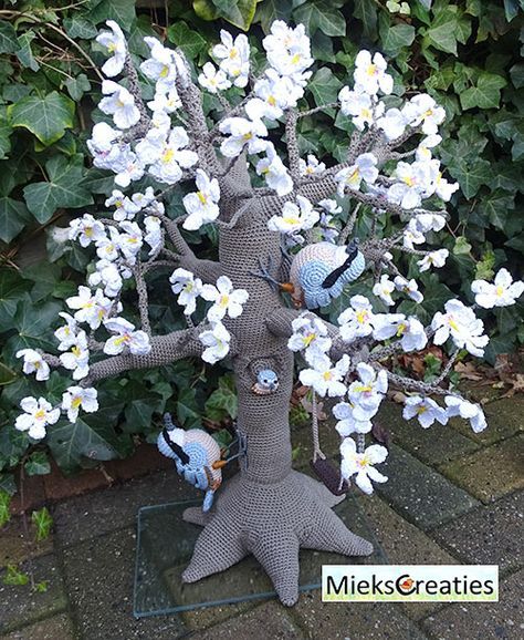 a tree with white flowers and two blue birds sitting on it's branches in front of some bushes