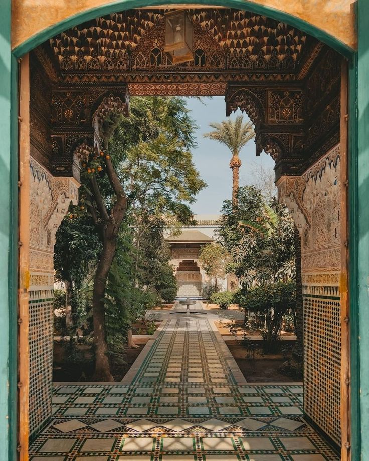 an archway leading into a courtyard with tiled floors and trees on either side, in front of a palm tree