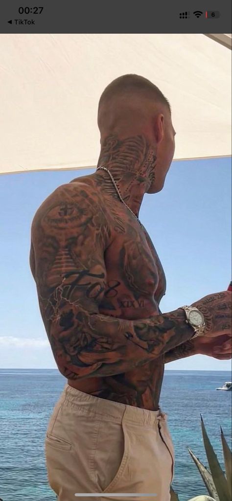 a man with tattoos on his arm and chest standing next to an umbrella near the ocean