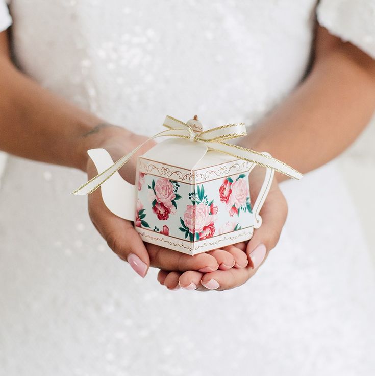 a person holding a small box with flowers on it and a bow around the top