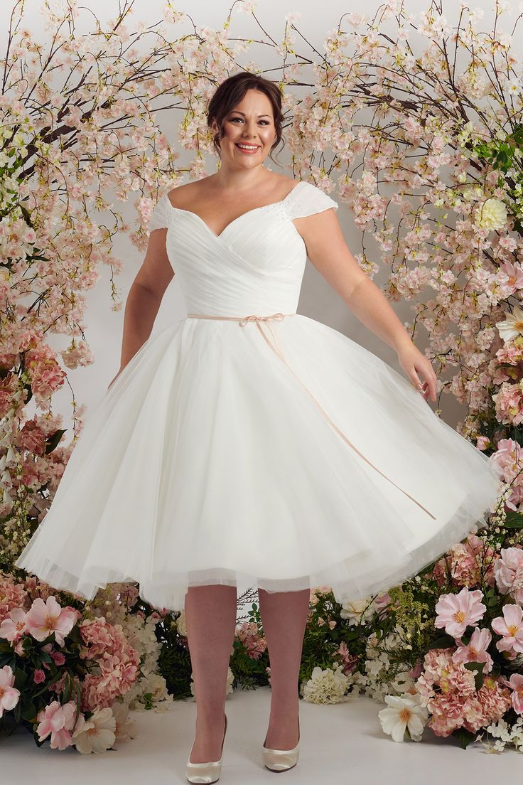 a woman in a white dress posing for the camera with pink flowers behind her,