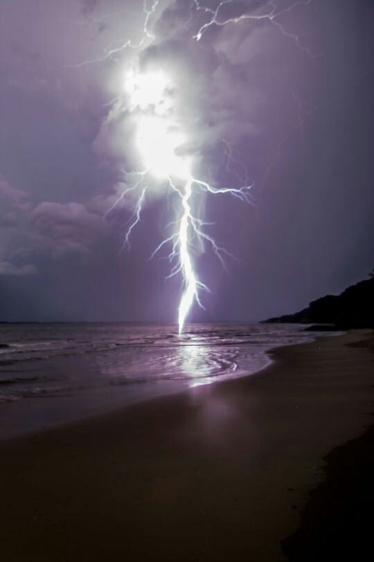 a lightning bolt hitting over the ocean on a beach at night with clouds in the background