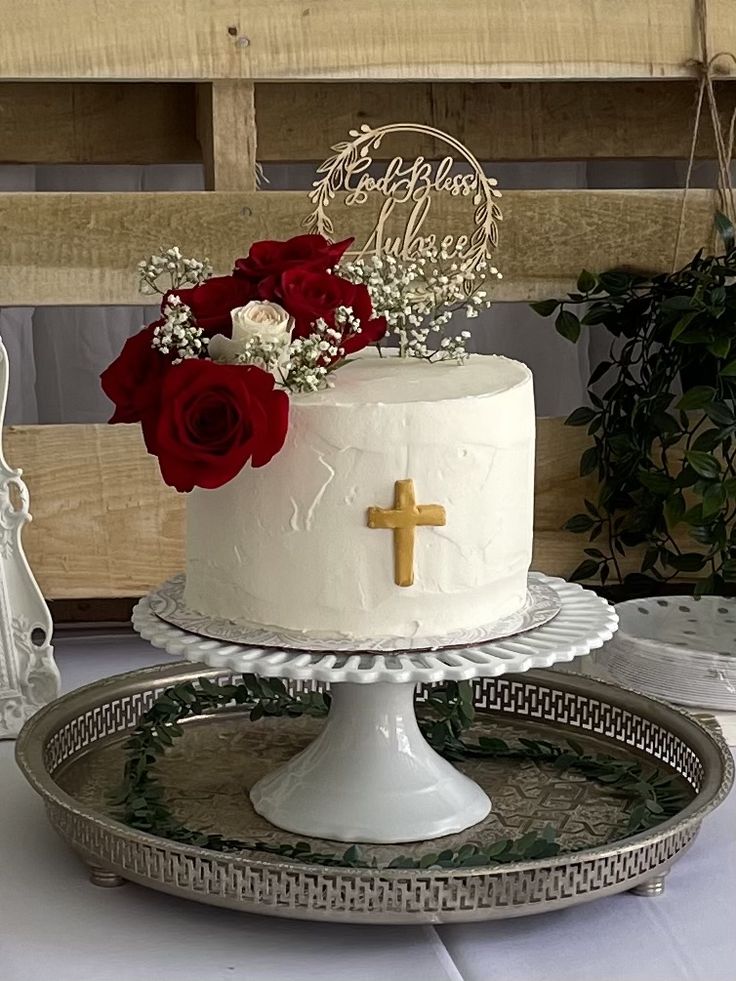 a white cake with red flowers and a cross on top is sitting on a silver platter