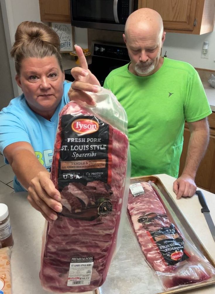 two people standing around a counter with some food on it and one person pointing at the camera