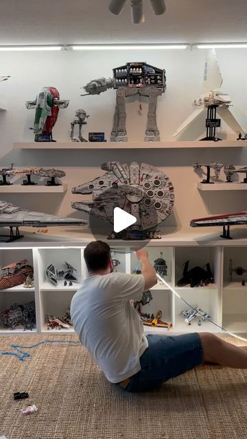 a man sitting on the floor in front of a shelf filled with toys