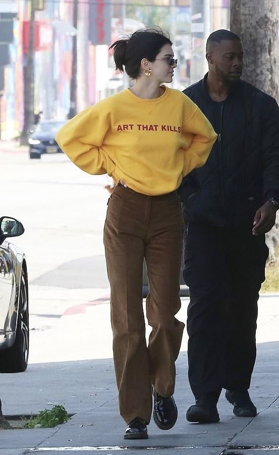 a woman in a yellow shirt and brown pants is walking down the street with a man