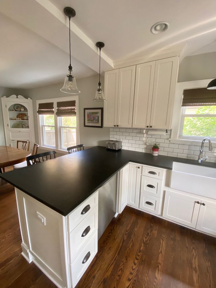 a large kitchen with white cabinets and black counter tops is pictured in this image, there are two windows on the far wall