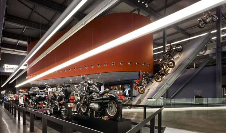 several motorcycles are on display in a building with glass railings and red curved wall