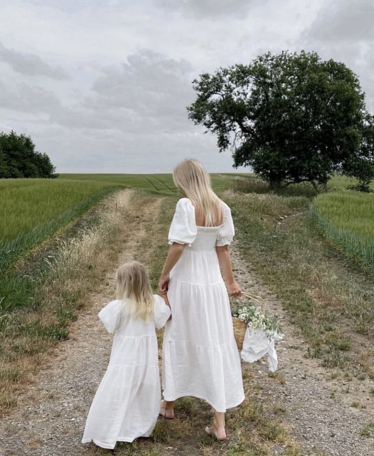 two women in white dresses walking down a dirt road