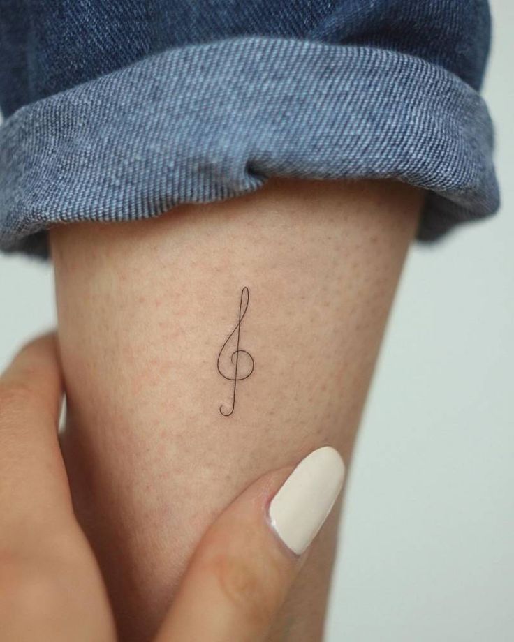 a woman's hand with a small tattoo on her left arm and the word music written in cursive writing