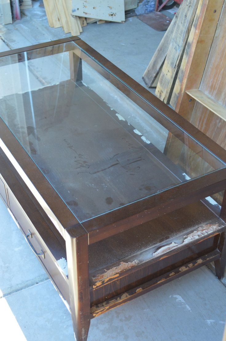 a glass and metal table sitting on top of a cement floor next to wooden boards