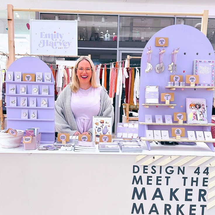 a woman standing in front of a table with items on it and a sign that says design 4 meet the maker market