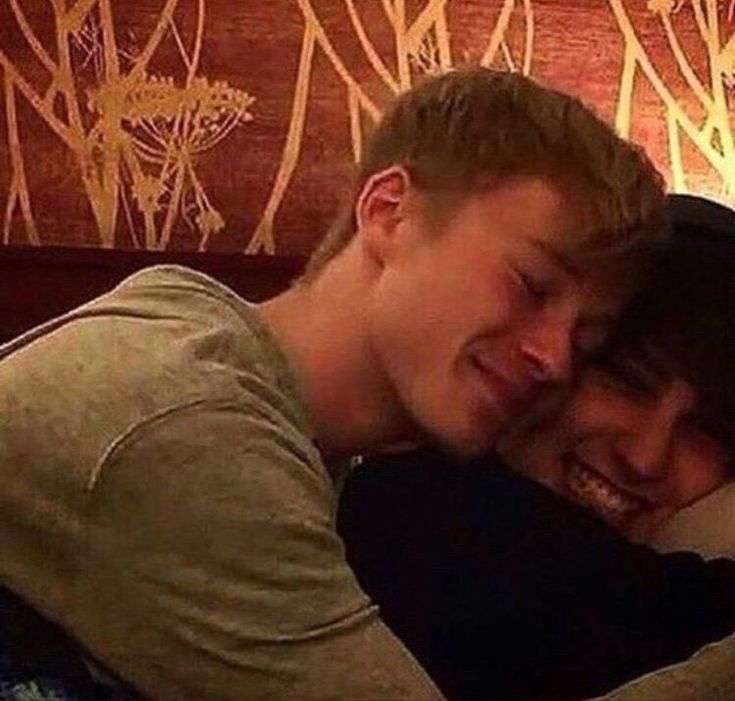 a man and woman cuddle together in front of a wallpapered headboard