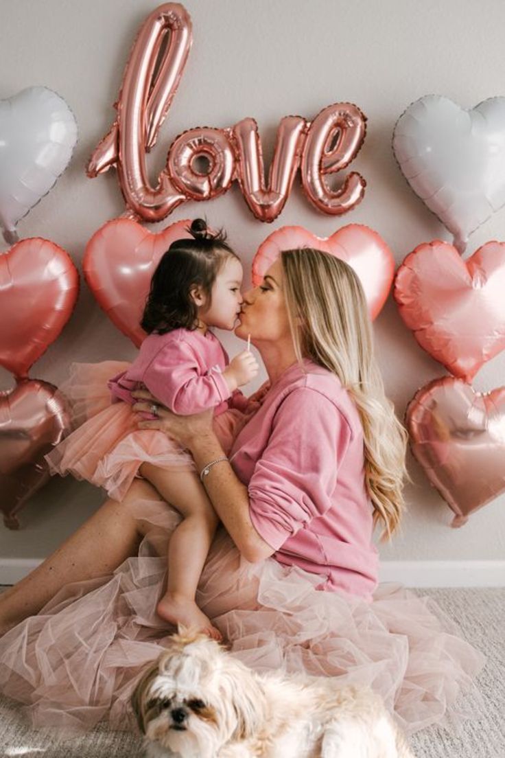 a mother and daughter sitting on the floor in front of balloons that say love with heart shaped balloons behind them