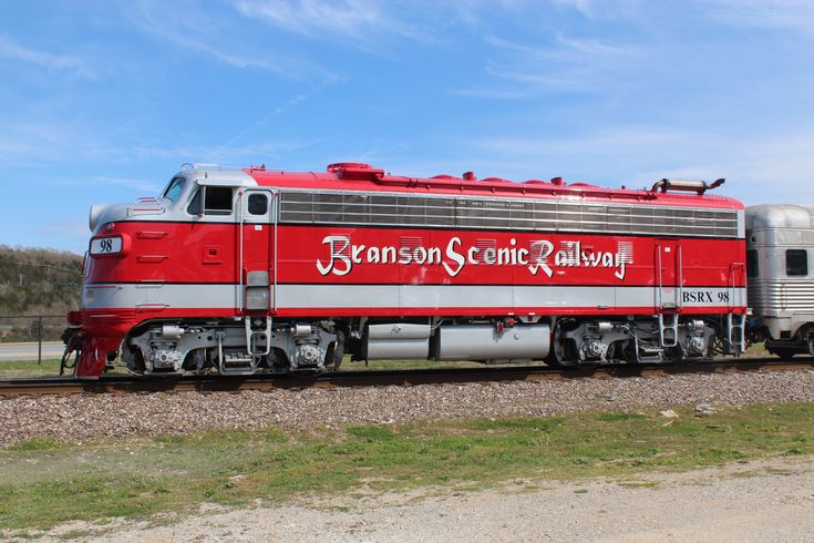 a red and silver train traveling down tracks next to a lush green field on a sunny day