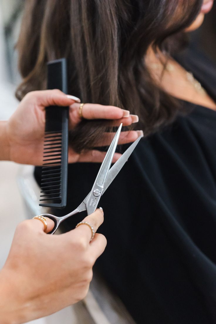 a woman cutting another person's hair with a pair of scissors and combs