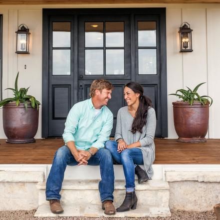 a man and woman are sitting on the steps in front of a house with potted plants