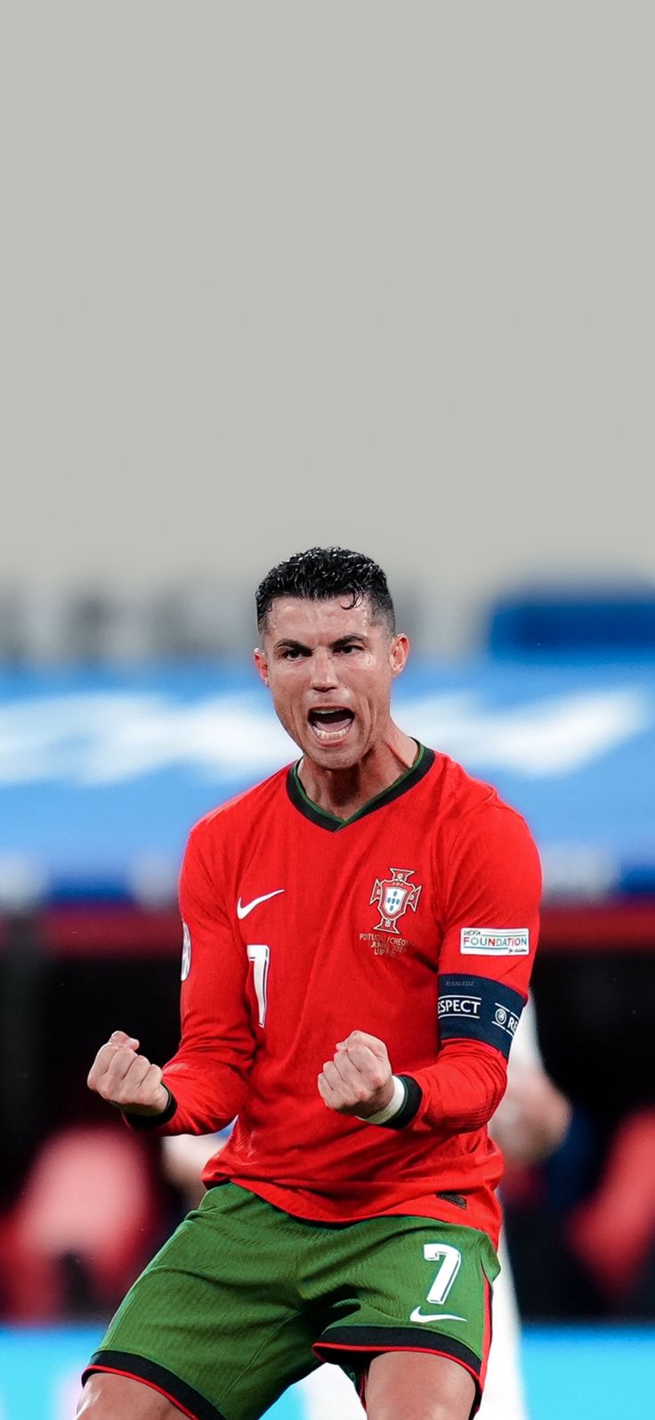 a soccer player with his mouth wide open in front of the camera, wearing green shorts and a red shirt