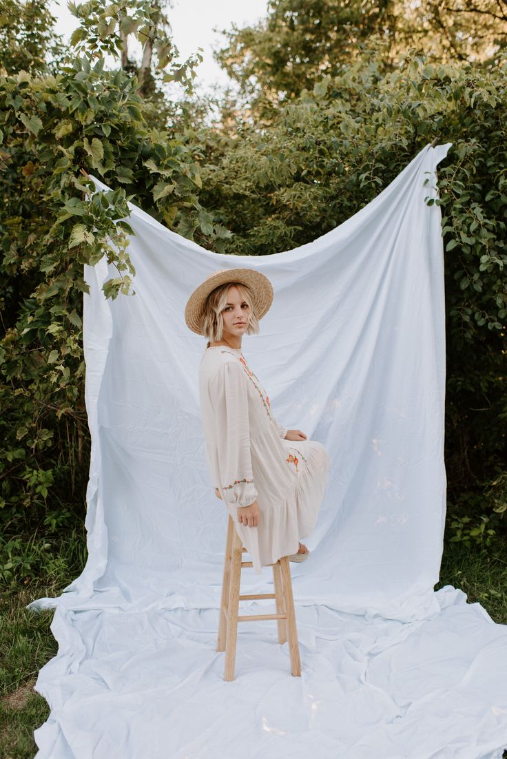 a woman sitting on a stool in front of a white cloth draped over her head