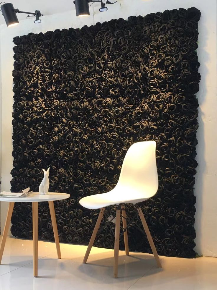 two white chairs sitting next to each other in front of a black wall with flowers on it