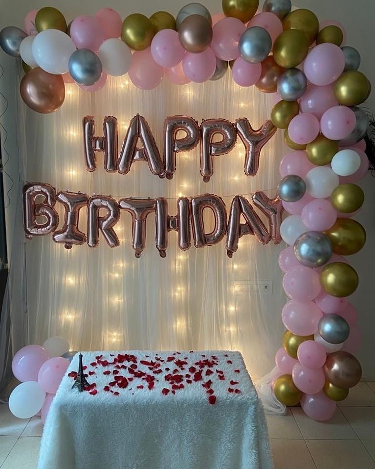 a birthday party with balloons and streamers in the shape of a heart on a table