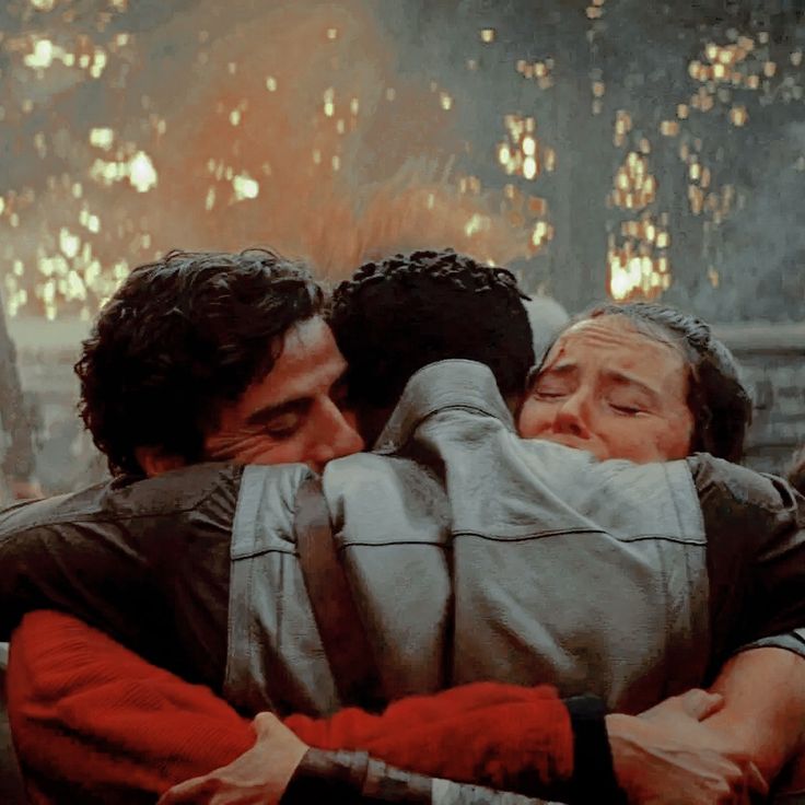 two men hugging each other in the middle of an outdoor area with trees and lights behind them