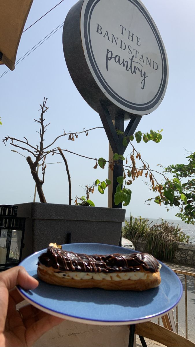 a person holding a plate with a donut on it in front of a sign