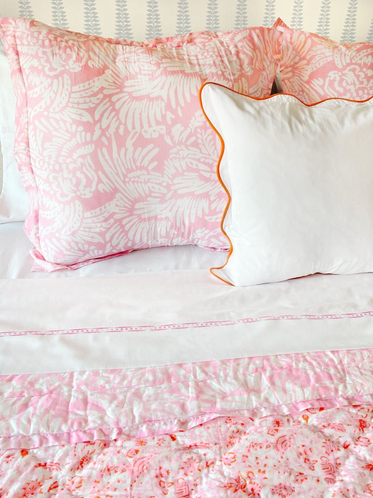 a bed with pink and white comforter, two pillows on the headboard and one pillow in the middle