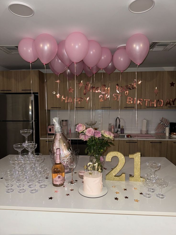 a table topped with champagne glasses and balloons next to a bottle of wine on top of a counter