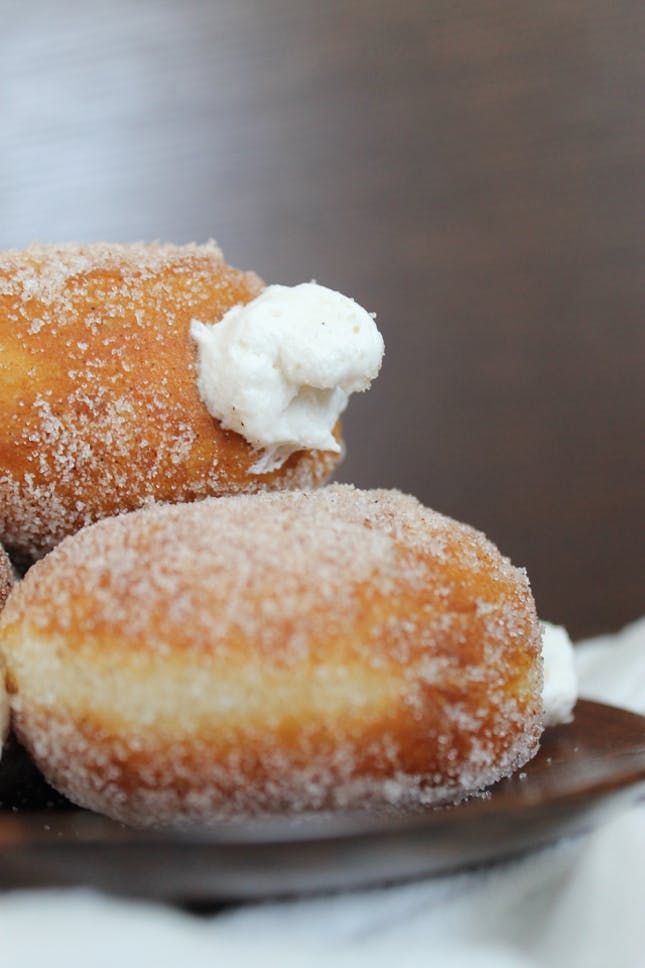 three donuts on a plate covered in powdered sugar and icing with whipped cream