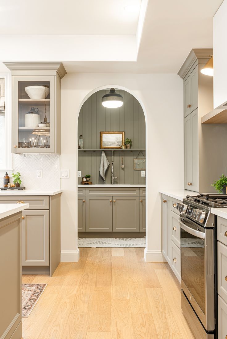 a kitchen with an arched doorway leading into the dining room and kitchen area, along with white cabinets and light wood flooring