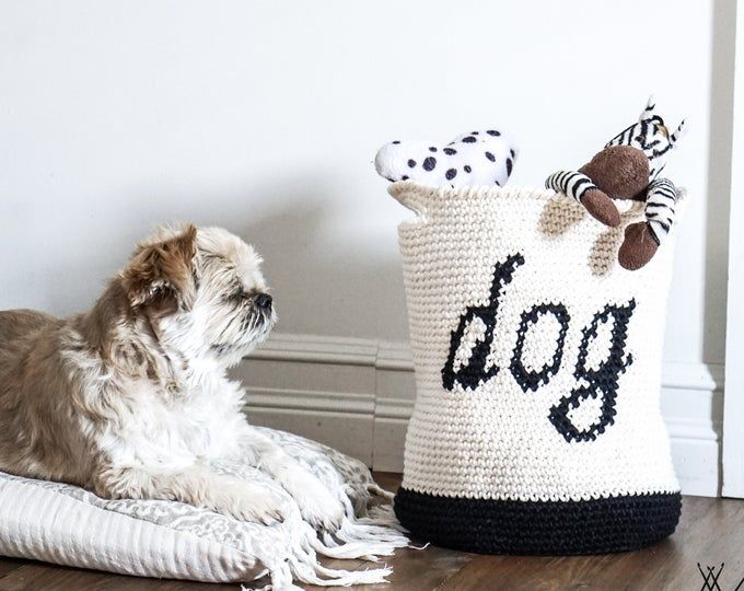 a dog laying on the floor next to a crocheted bag and stuffed animal