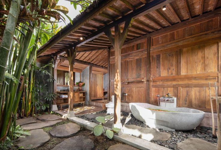 a bathtub sitting under a wooden roof next to a lush green plant filled garden