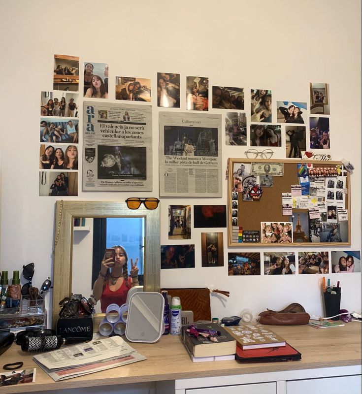 a cluttered desk with many pictures on the wall and a mirror above it that is covered in photos