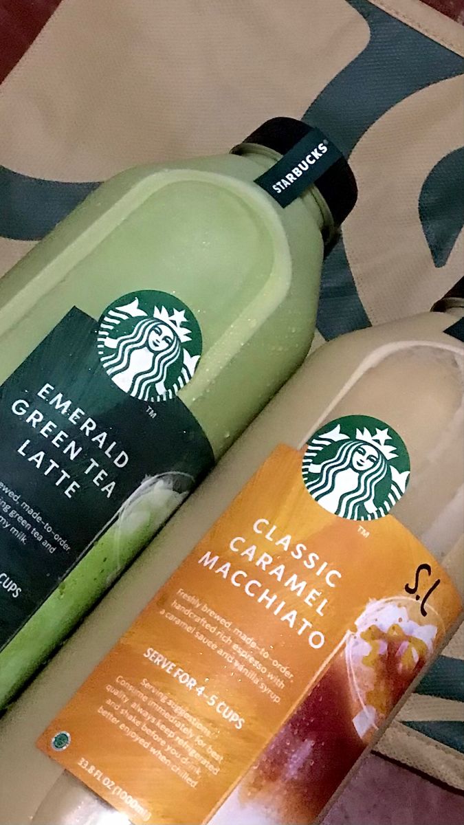 two starbucks drinks sitting on top of a bed next to each other, one is green and the other is orange