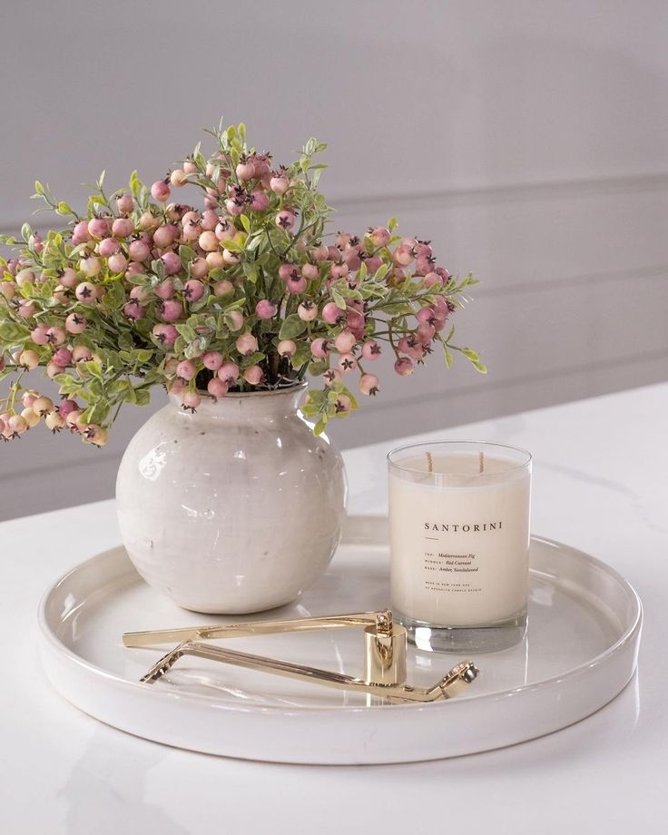 a white vase filled with flowers next to a candle on top of a tray that is sitting on a table