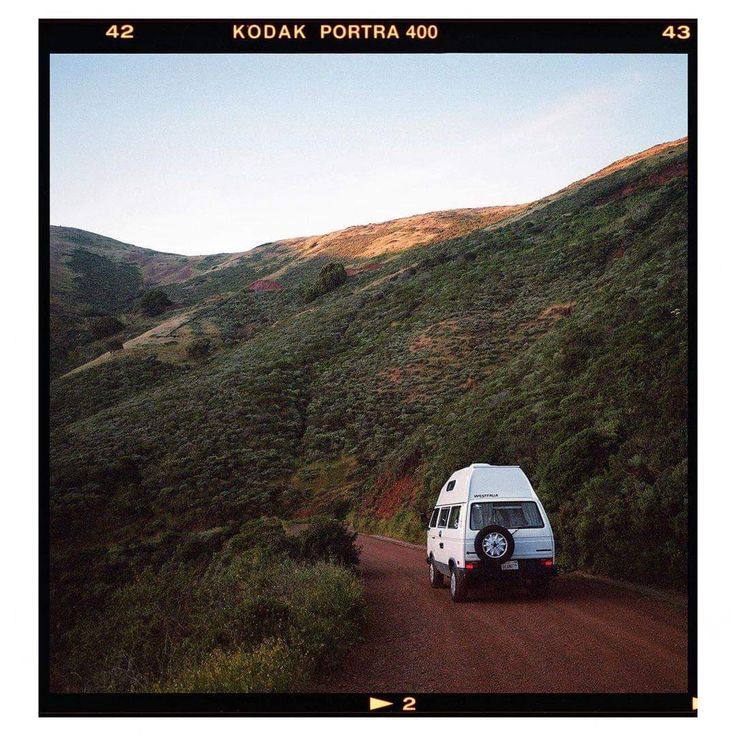 a van is parked on the side of a dirt road with hills in the background