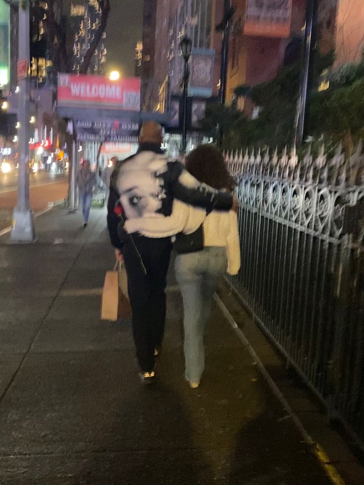 two people walking down the street at night with their backs to each other, carrying bags