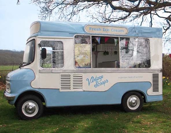 a blue and white food truck parked on top of a grass covered field next to a tree