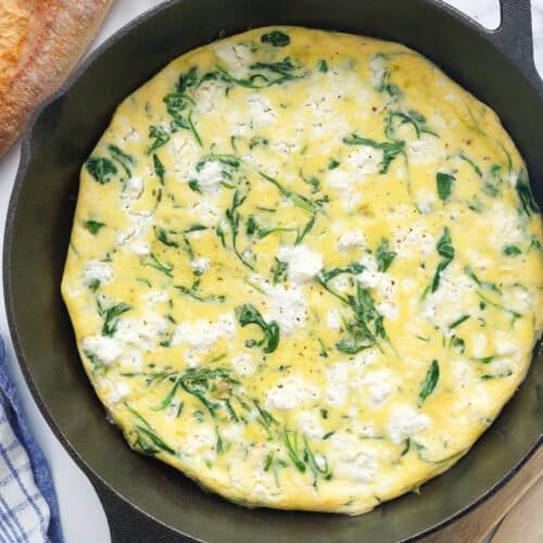 an omelet with spinach and cheese in a skillet next to bread