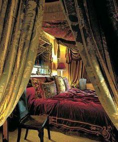 the canopy bed is made up with red sheets and drapes on it's sides