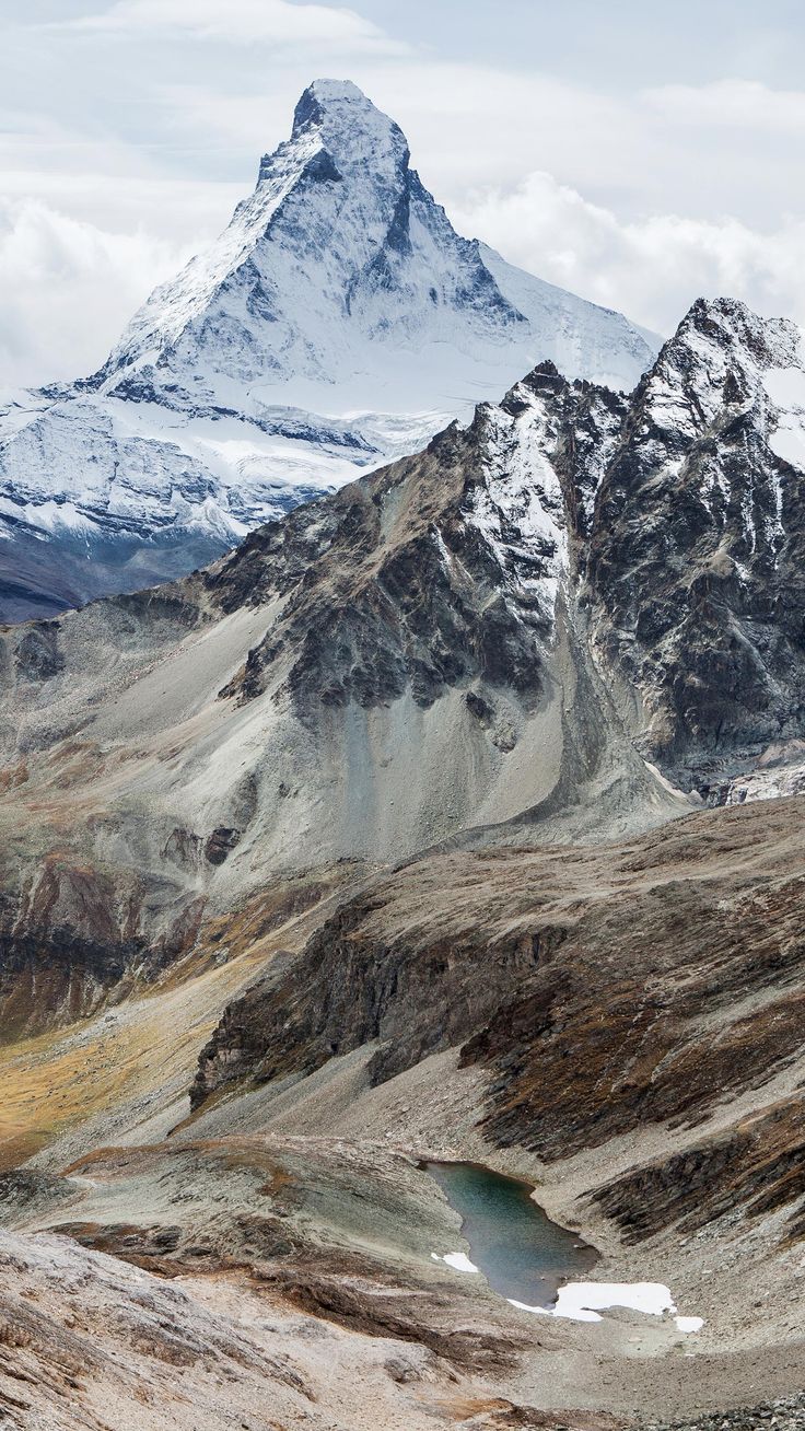 the mountains are covered in snow and brown grass, with a small lake below them