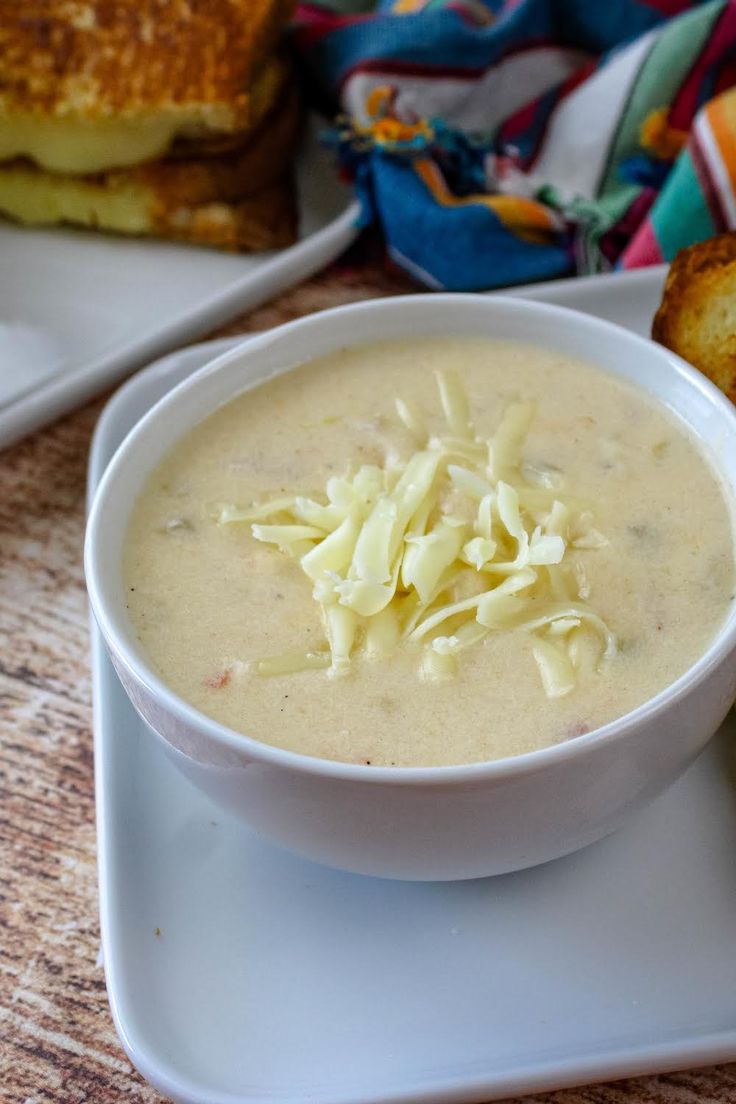 a bowl of soup on a plate next to grilled cheese