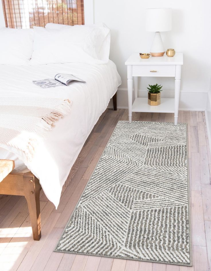 a white bed sitting next to a wooden table on top of a hard wood floor