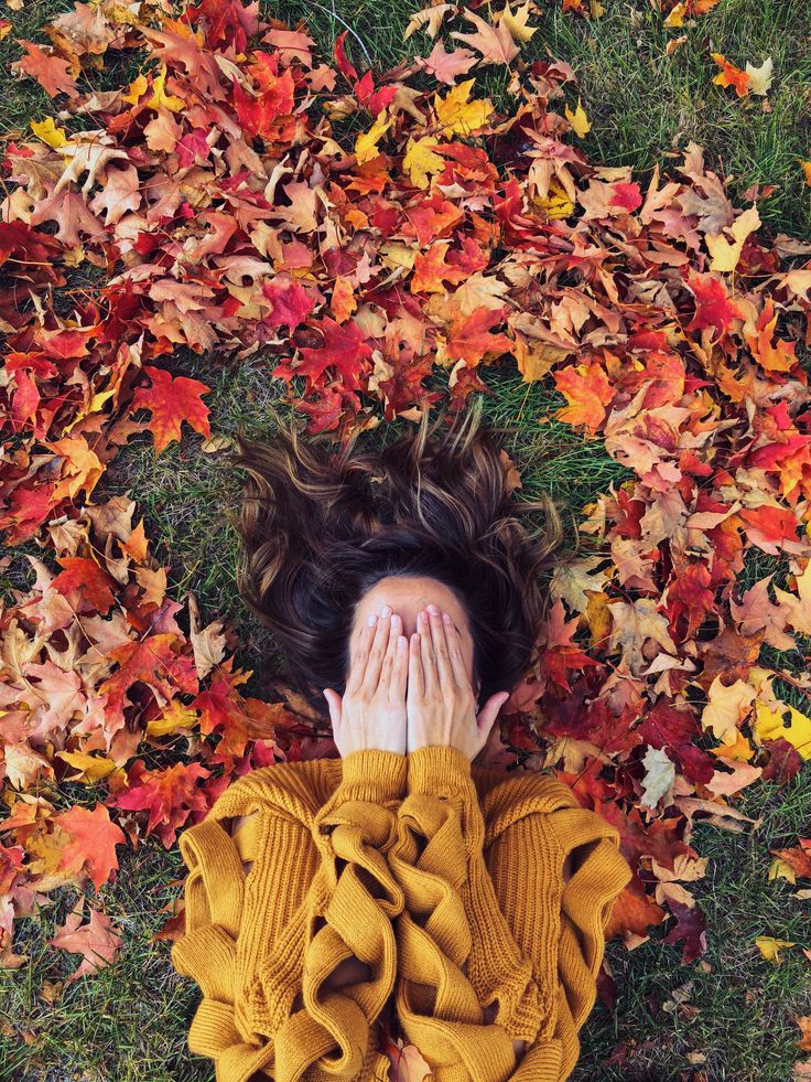 a woman laying on the ground covered in leaves covering her face and hands with both hands