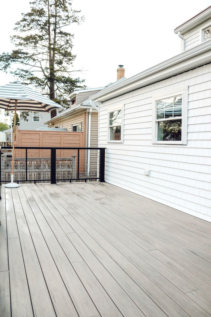 a wooden deck with an umbrella over it and a white house in the back ground