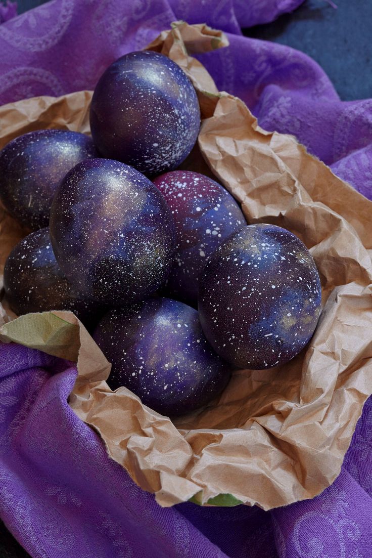 some purple eggs are in a bowl on a purple cloth with gold speckles